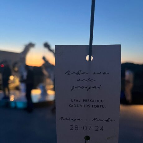 Hand holding a thank you note at sunset with blurred background of boats and water.