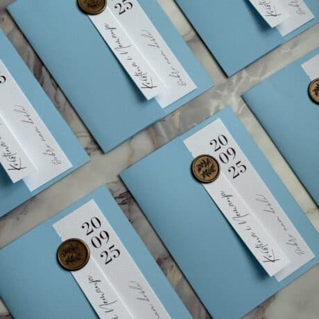 Stylish wedding invitation card with blue background, white ribbon, and gold wax seal for elegant ce.