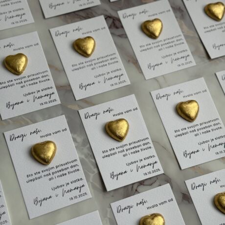 Golden heart-shaped chocolates on personalized thank you cards for "Zahvalnica M50" event.