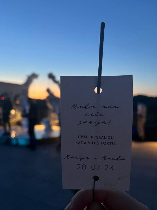 Hand holding a thank you note at sunset with blurred background of boats and water.