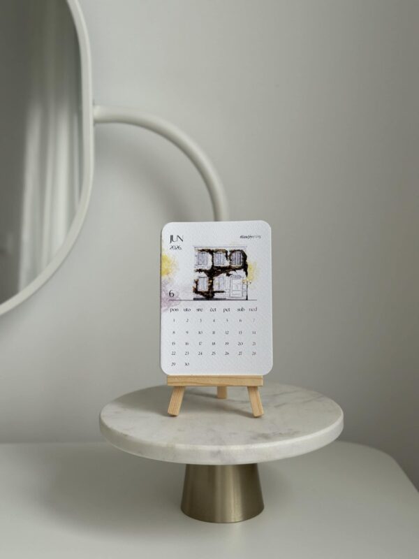 Elegant home decor tabletop calendar display on miniature easel with artistic building illustration, minimalist interior design.