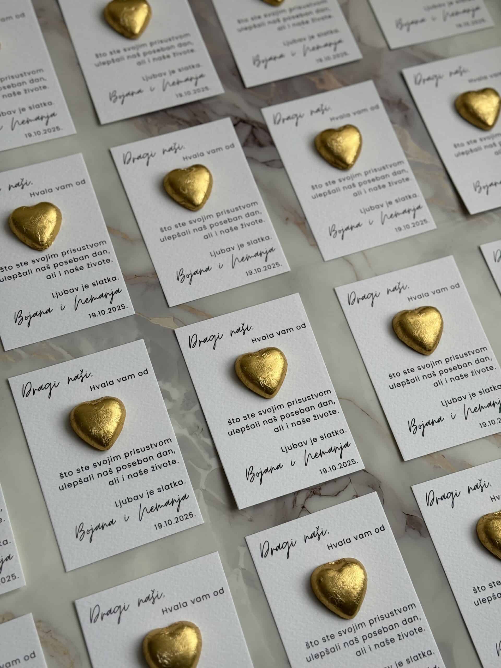 Golden heart-shaped chocolates on personalized thank you cards for "Zahvalnica M50" event.